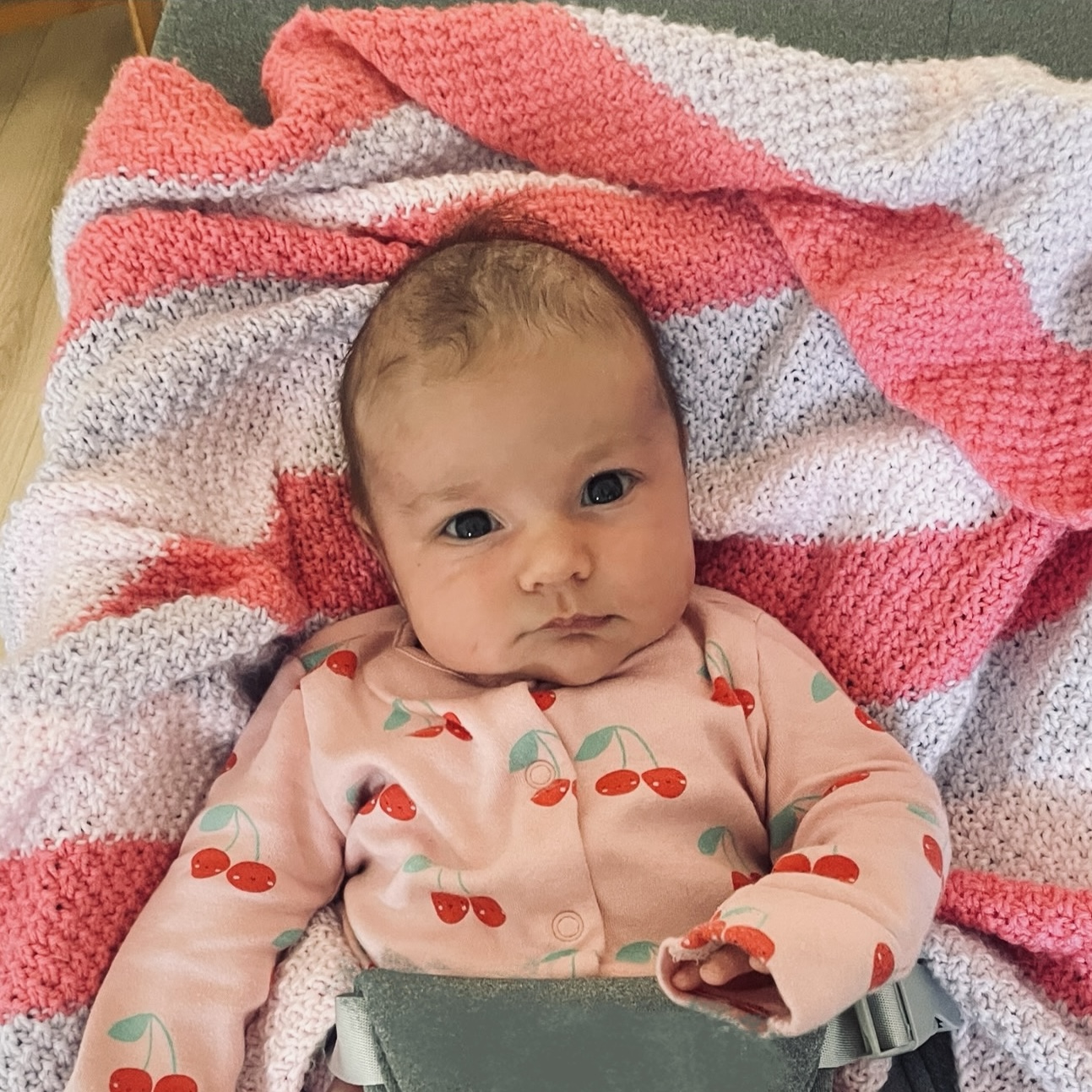 Baby Edith laying on her back on a blanket wearing a pink onesie